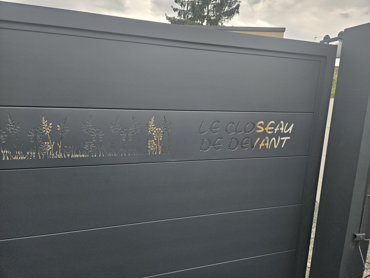 Portail coulissant en aluminium, remplissage en lames avec un habillage décoratif "fleurs" + inscription adresse. Laquage ral 7016 FT 53600 CHATRES LA FORET
