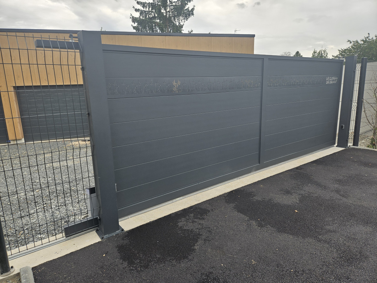 Portail coulissant en aluminium, remplissage en lames avec un habillage décoratif "fleurs" + inscription adresse. Laquage ral 7016 FT 53600 CHATRES LA FORET