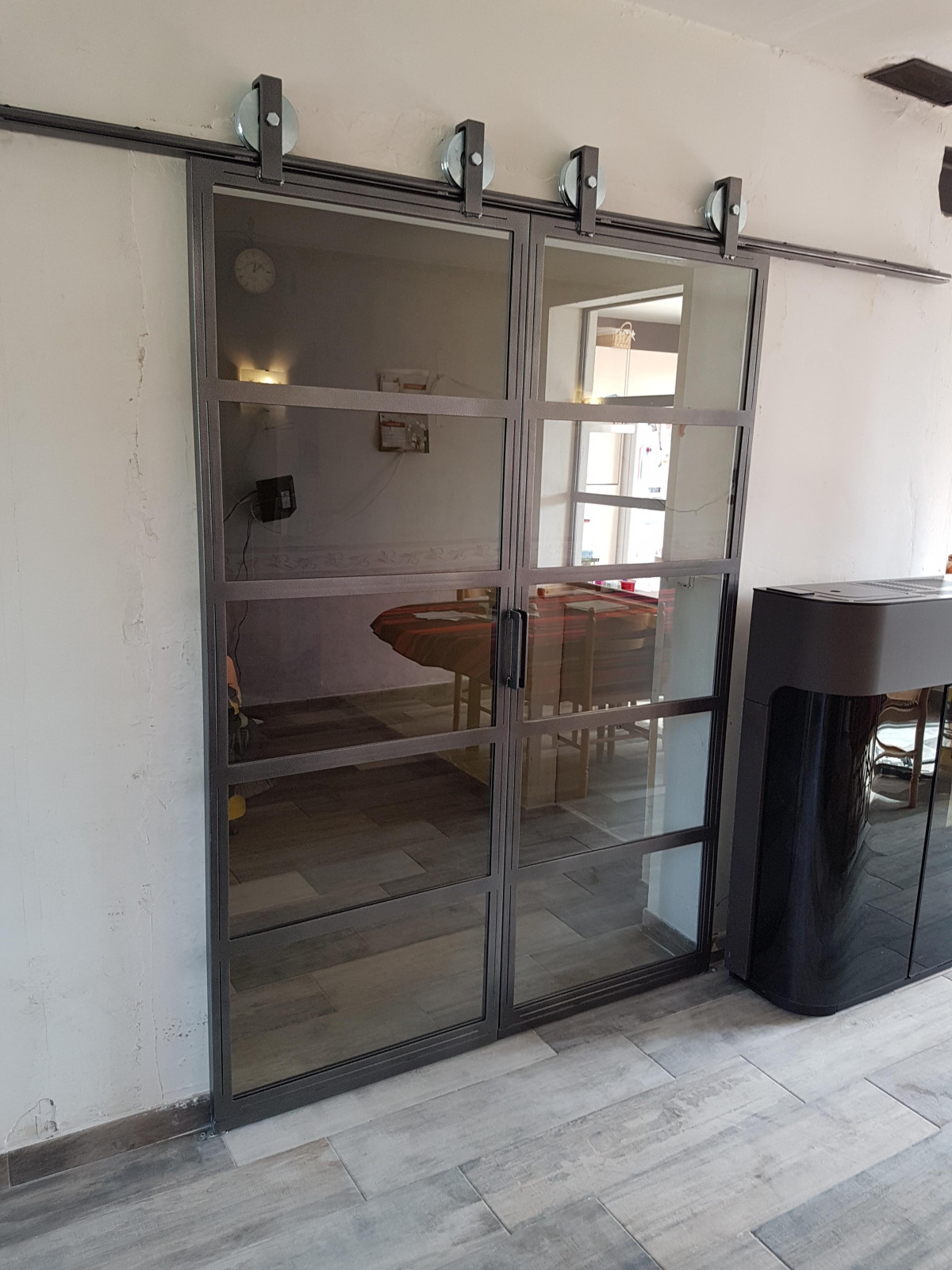 Double porte verrière coulissante en acier, avec traverse horizontale, verre 33/2 feuilletés, avec roulettes apparentes.