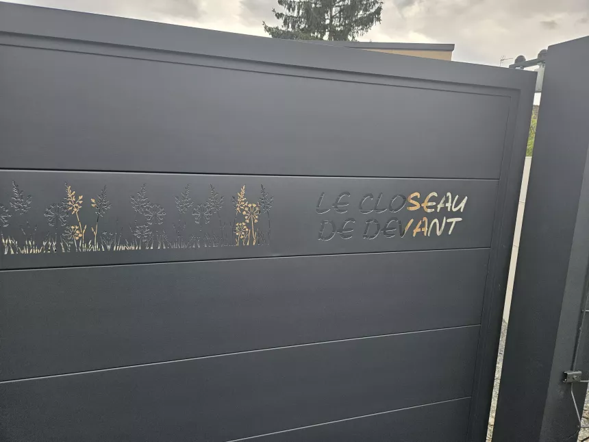 Portail coulissant en aluminium, remplissage en lames avec un habillage décoratif "fleurs" + inscription adresse. Laquage ral 7016 FT 53600 CHATRES LA FORET