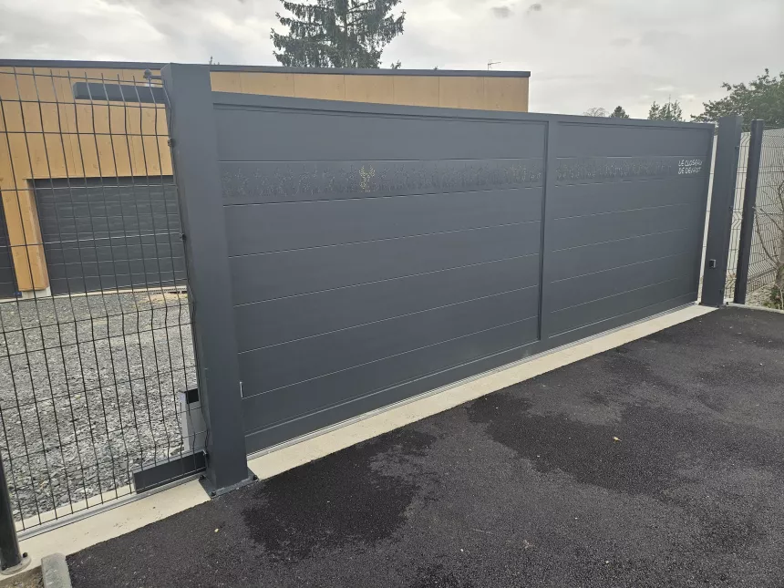 Portail coulissant en aluminium, remplissage en lames avec un habillage décoratif "fleurs" + inscription adresse. Laquage ral 7016 FT 53600 CHATRES LA FORET