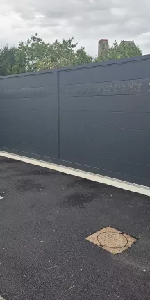 Portail coulissant en aluminium, remplissage en lames avec un habillage décoratif "fleurs" + inscription adresse. Laquage ral 7016 FT 53600 CHATRES LA FORET