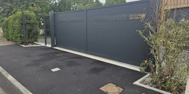 Portail coulissant en aluminium, remplissage en lames avec un habillage décoratif "fleurs" + inscription adresse. Laquage ral 7016 FT 53600 CHATRES LA FORET