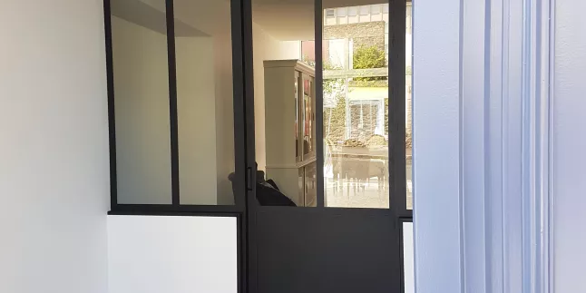 Verrière + porte ouvrante en aluminium, avec traverse intermédiaire, verre clair en 33/2 feuilleté, soubassement en tôle pour la porte, laquage ral noir 9005 FT.